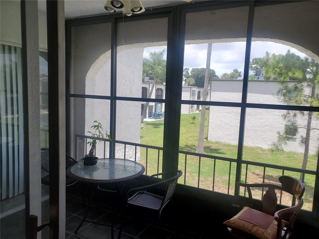 A screened-in patio features a glass-top table, chairs, and views of a grassy courtyard — 7701 STARKEY ROAD UNIT 324, SEMINOLE, FL