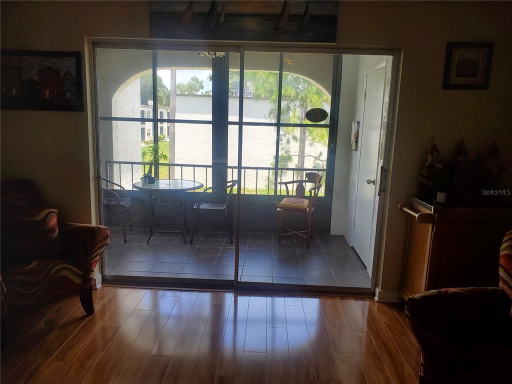 A living room with hardwood floors looks out through sliding glass doors to a screened balcony — 7701 STARKEY ROAD UNIT 324, SEMINOLE, FL