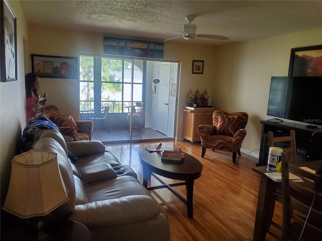 A living room features hardwood floors, a leather sofa, patterned armchairs, and a sliding glass door — 7701 STARKEY ROAD UNIT 324, SEMINOLE, FL