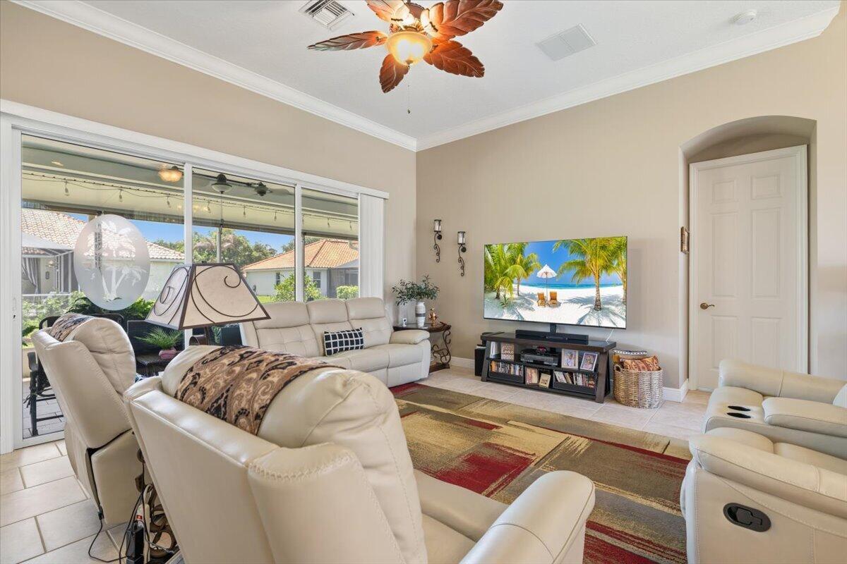 A living room features light-colored leather furniture, a television, and large sliding glass doors — 5828 Pine Ridge Circle, Vero Beach FL 32967, VERO BEACH, FL