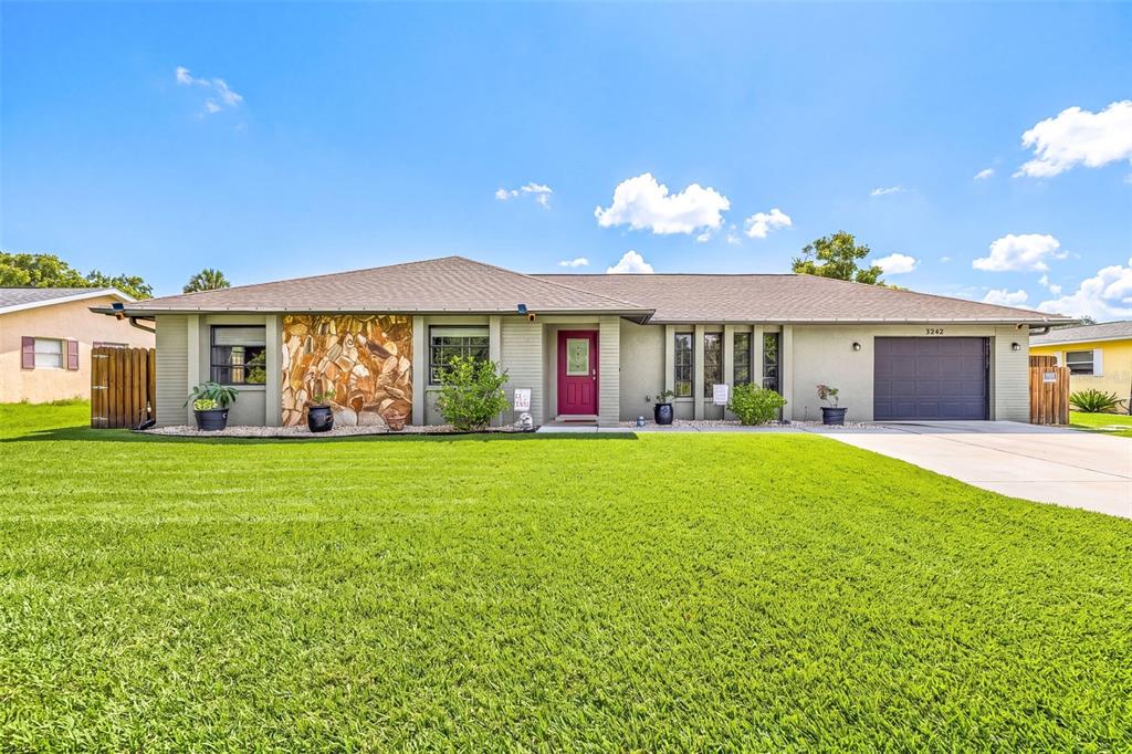 A single-story house with a stone accent wall, a red front door, and a garage — 3242 CARDIFF ST, PUNTA GORDA, FL