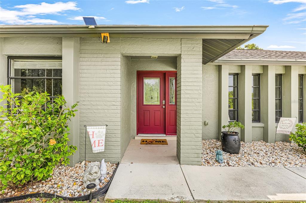 The exterior of a house features a red front door, green brick walls, and landscaping — 3242 CARDIFF ST, PUNTA GORDA, FL