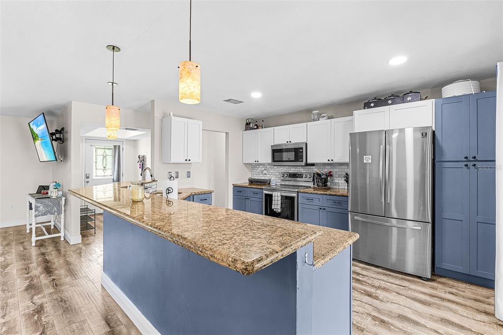A kitchen features blue lower cabinets, white upper cabinets, granite countertops, and stainless steel appliances — 3242 CARDIFF ST, PUNTA GORDA, FL
