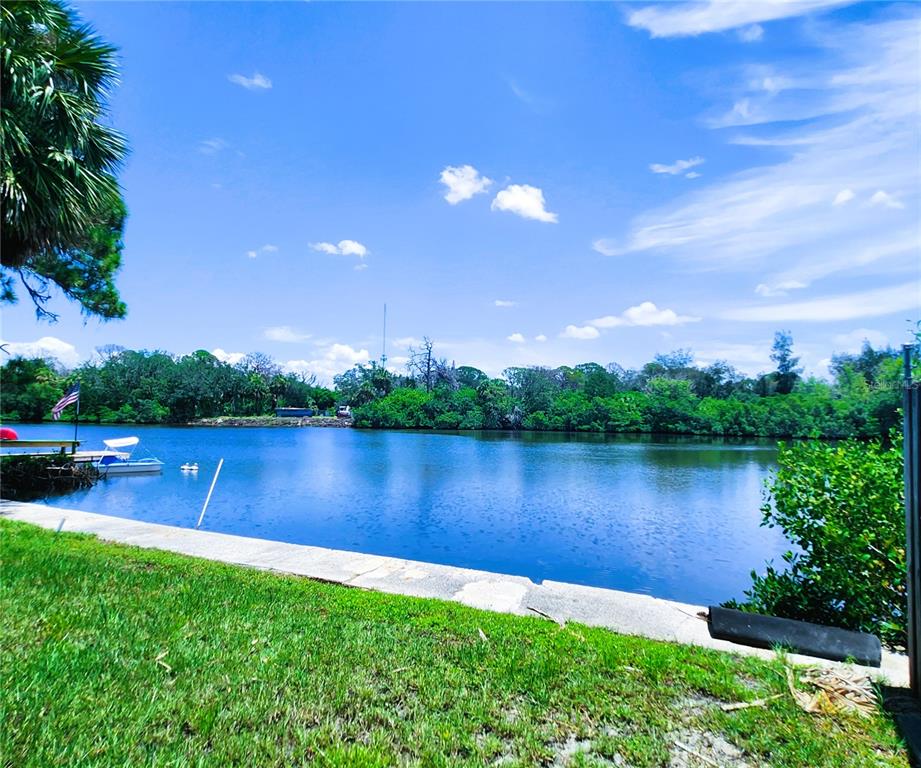 A concrete seawall borders a grassy lawn overlooking a calm canal with a small boat — 6975 EDGEWATER DRIVE, NEW PORT RICHEY, FL