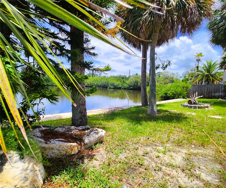 A grassy backyard features palm trees, a stone fire pit, and a view of water — 6975 EDGEWATER DRIVE, NEW PORT RICHEY, FL