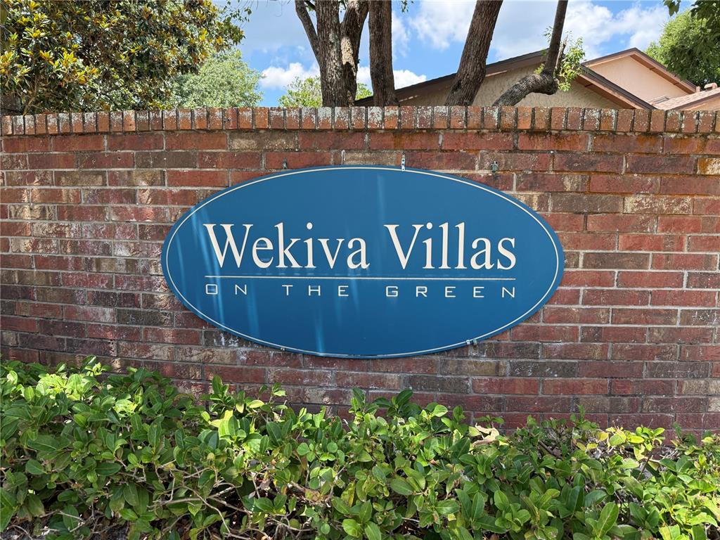 A blue oval sign reading Wekiva Villas on the Green is mounted on a brick wall — 335 GOLFSIDE COVE, LONGWOOD, FL