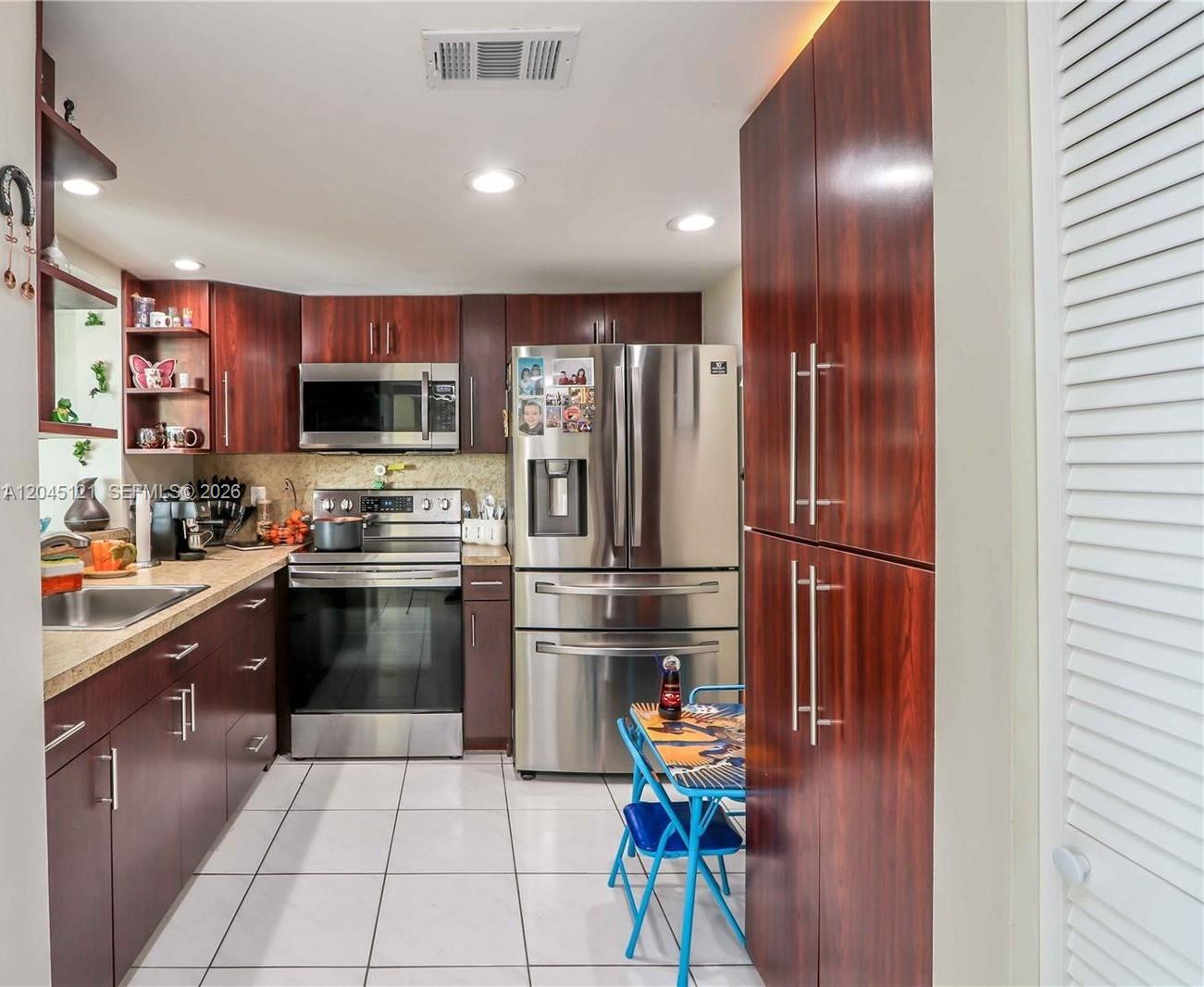 A kitchen features dark wood cabinets, stainless steel appliances, and white tiled flooring — 2055 SW 122nd Ave # 306, Miami FL 33175, MIAMI, FL