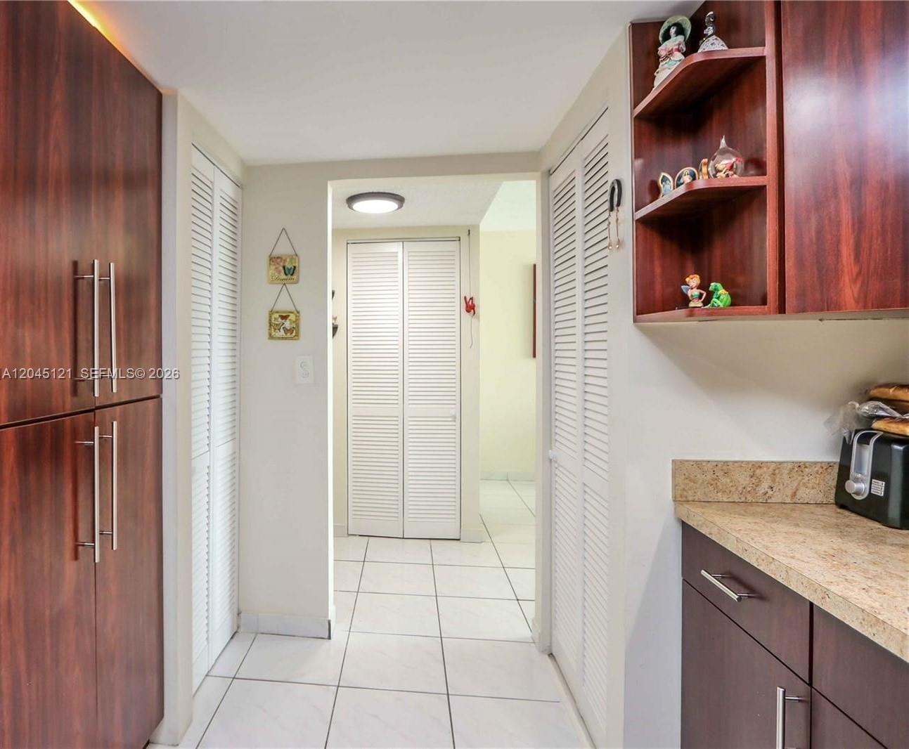 A kitchen hallway features dark wood cabinetry, white louvered closet doors, and light tile flooring — 2055 SW 122nd Ave # 306, Miami FL 33175, MIAMI, FL