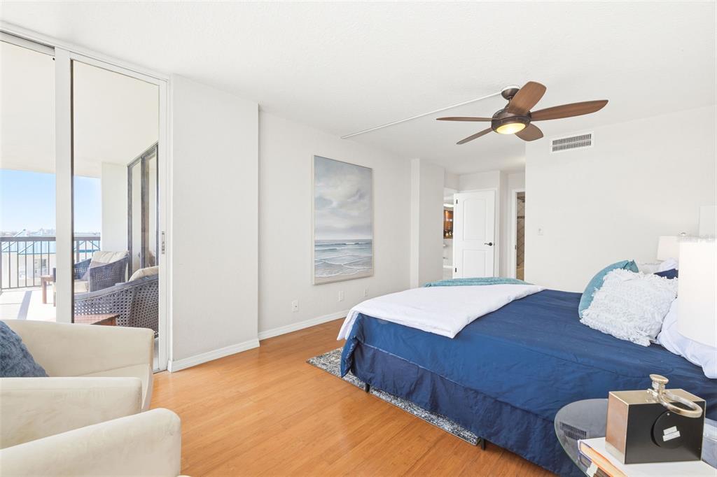 A bedroom features hardwood floors, a ceiling fan, a blue bed, and a balcony view — 9415 BLIND PASS ROAD UNIT 806, ST PETE BEACH, FL