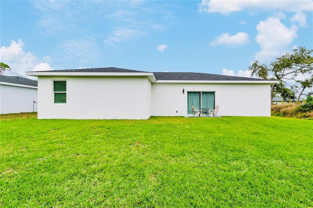 The back exterior of a white single-story house with a lawn and sliding glass doors — 189 STATLER STREET, PORT CHARLOTTE, FL