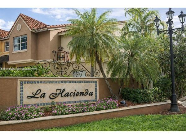 The exterior of a residential community entrance sign features palm trees and a street lamp — 18304 NW 68th Ave # C, Hialeah FL 33015, HIALEAH, FL
