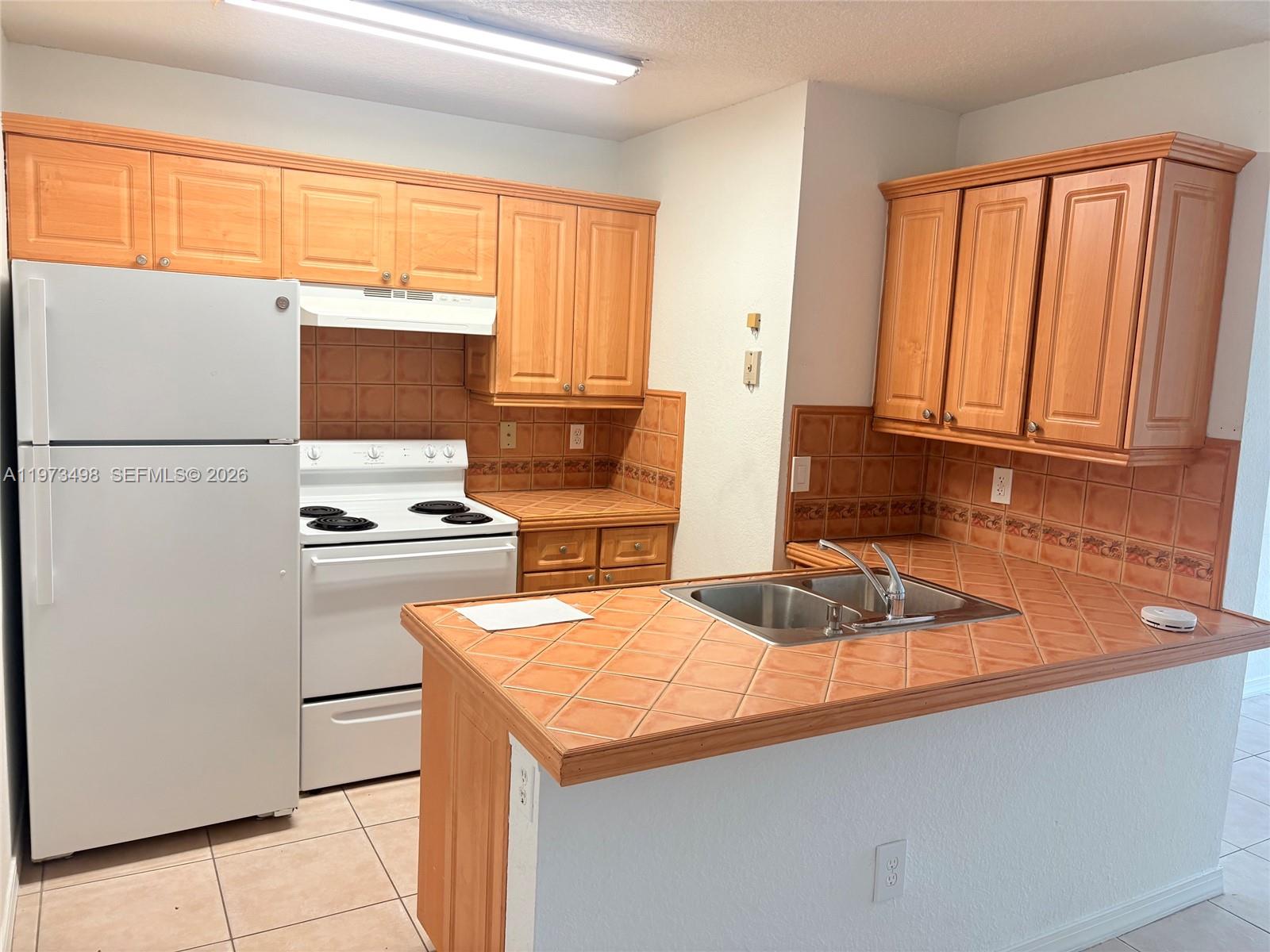 A kitchen features light wood cabinets, tiled countertops, and white appliances — 18304 NW 68th Ave # C, Hialeah FL 33015, HIALEAH, FL
