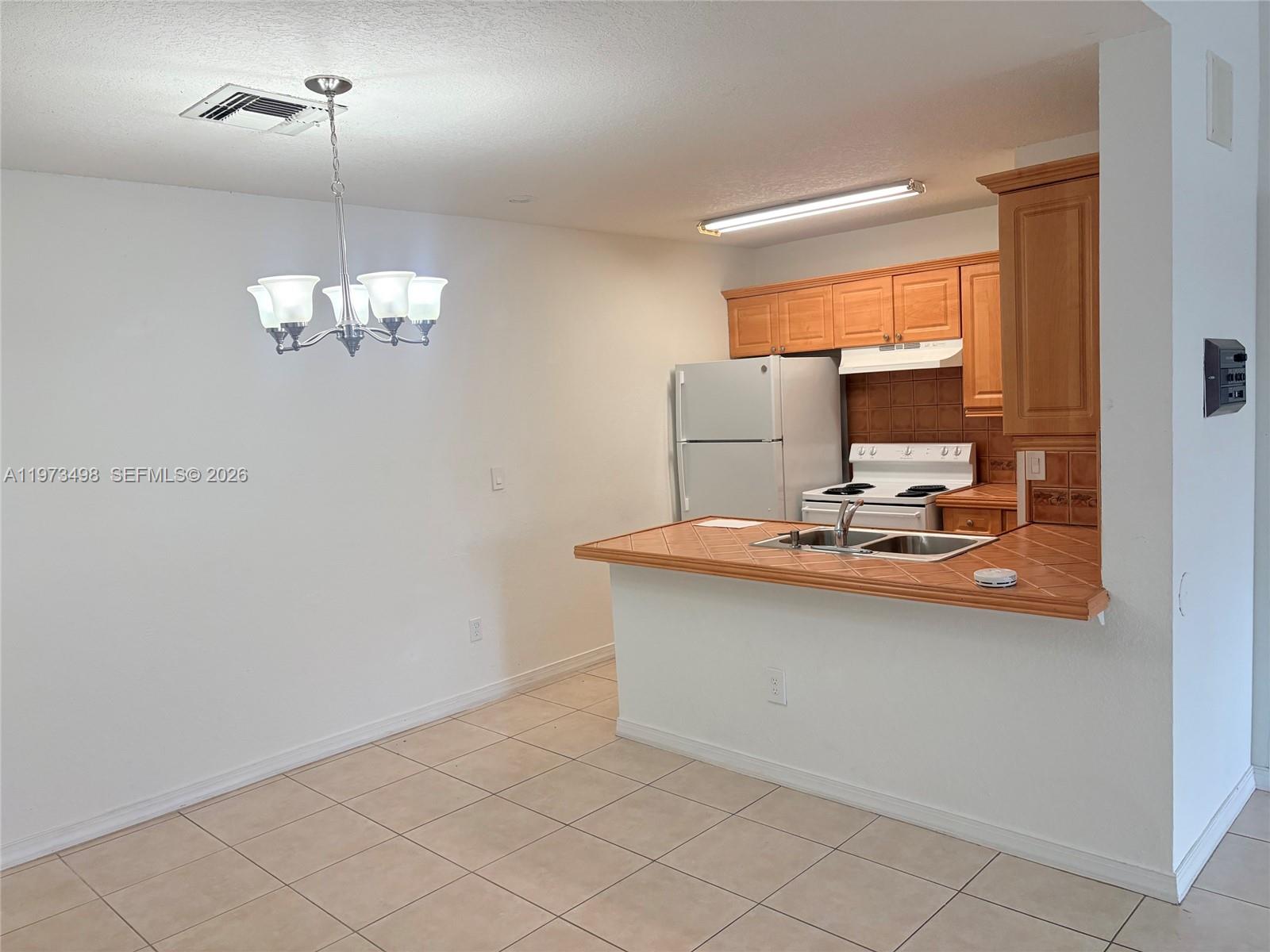 A kitchen with light wood cabinets and a tiled peninsula counter opens to a dining area — 18304 NW 68th Ave # C, Hialeah FL 33015, HIALEAH, FL