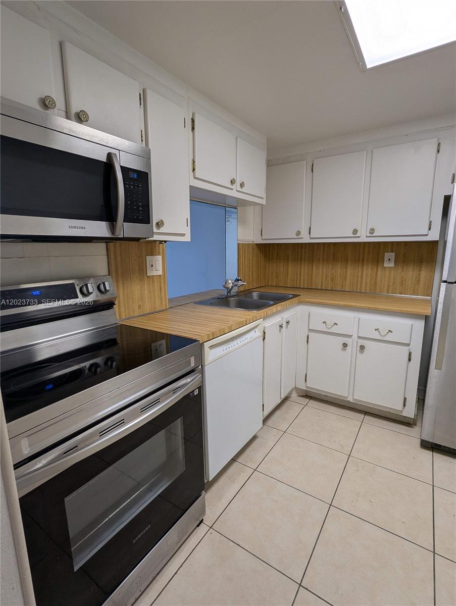 A kitchen features white cabinets, wood-look laminate countertops, stainless steel appliances, and beige tile flooring — 16751 NE 9th Ave # 408, North Miami Beach FL 33162, NORTH MIAMI BEACH, FL