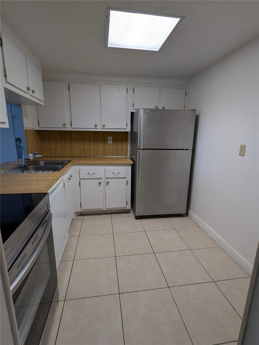A kitchen features white cabinets, a stainless steel refrigerator, and wood-look laminate countertops — 16751 NE 9th Ave # 408, North Miami Beach FL 33162, NORTH MIAMI BEACH, FL