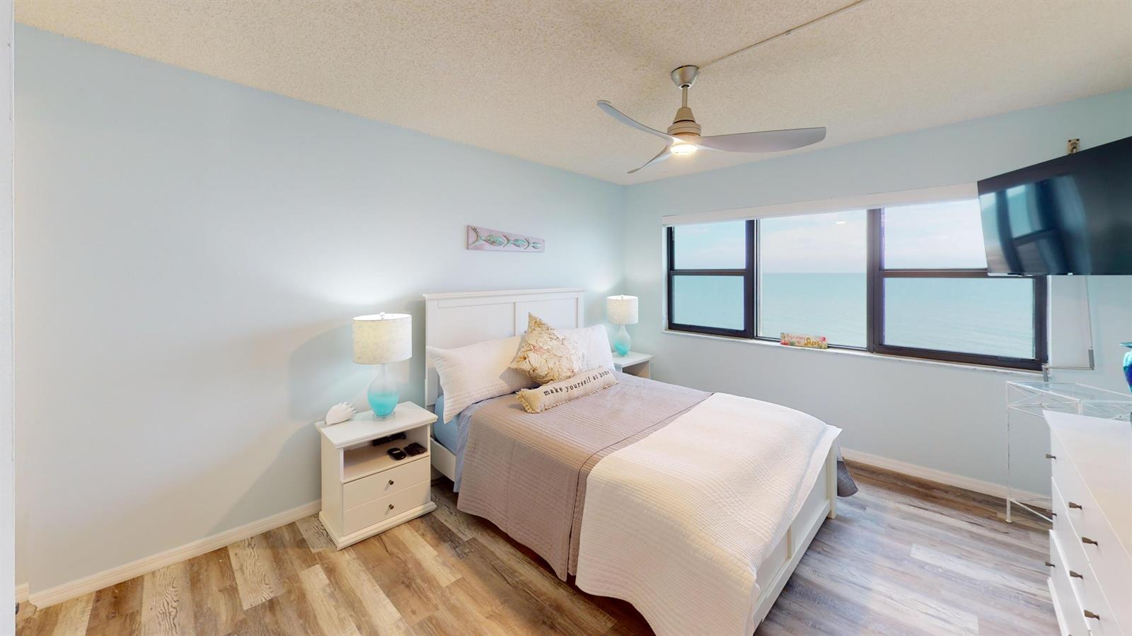 A bedroom with a bed, nightstands, ceiling fan, and a large window overlooking the ocean — 10044 S Ocean Drive # 805, Jensen Beach FL 34957, JENSEN BEACH, FL