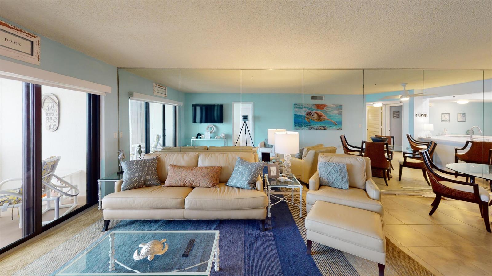 A living room features a beige sofa, matching armchair, glass coffee table, and mirrored walls — 10044 S Ocean Drive # 805, Jensen Beach FL 34957, JENSEN BEACH, FL