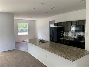 A kitchen with dark cabinets and granite countertops overlooks a carpeted living area — 3035 BREWSTER ROAD, NORTH PORT, FL