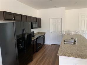 A kitchen features dark wood cabinets, black appliances, granite countertops, and a center island — 3035 BREWSTER ROAD, NORTH PORT, FL