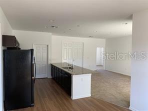 A kitchen with dark cabinets and a granite island overlooks an open carpeted living area — 3035 BREWSTER ROAD, NORTH PORT, FL