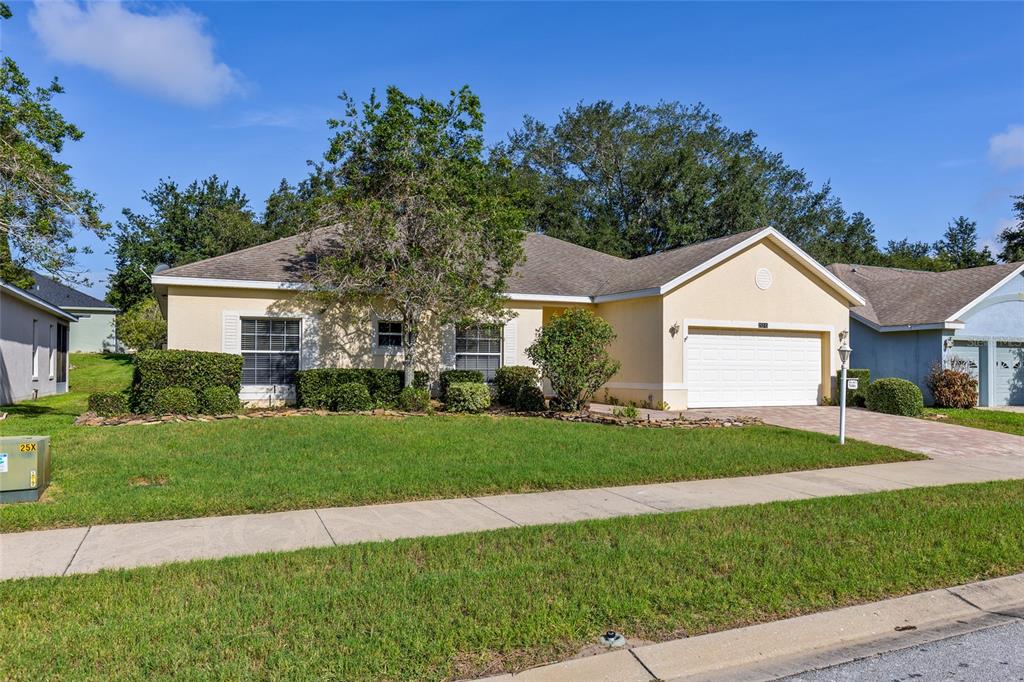 A single-story suburban house with a tan exterior, a two-car garage, and a front lawn — 25245 QUAIL CROFT PLACE, LEESBURG, FL
