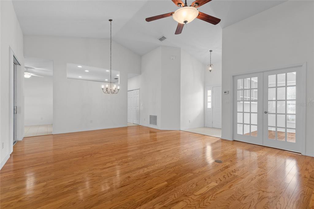 A spacious living room with vaulted ceilings, hardwood floors, a ceiling fan, and French doors — 25245 QUAIL CROFT PLACE, LEESBURG, FL