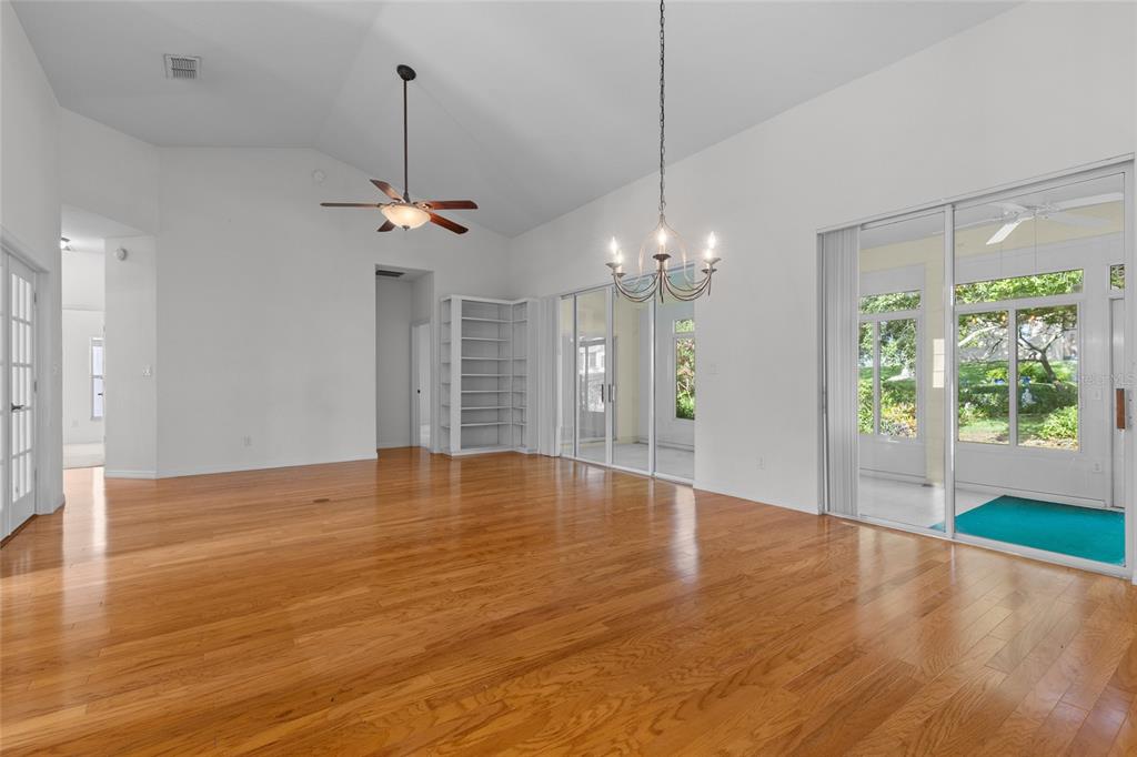 A spacious living room with hardwood floors, vaulted ceilings, a ceiling fan, and sliding glass doors — 25245 QUAIL CROFT PLACE, LEESBURG, FL