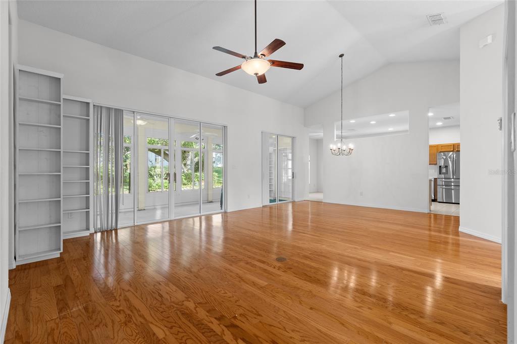 A spacious living room features hardwood floors, a vaulted ceiling, a ceiling fan, and bookshelves — 25245 QUAIL CROFT PLACE, LEESBURG, FL