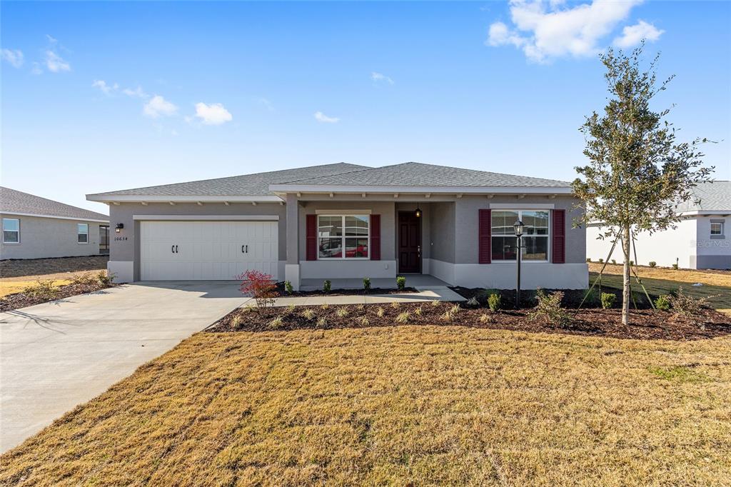A single-story house with a two-car garage, gray stucco exterior, and red window shutters — 10634 SW 101ST LANE ROAD, OCALA, FL