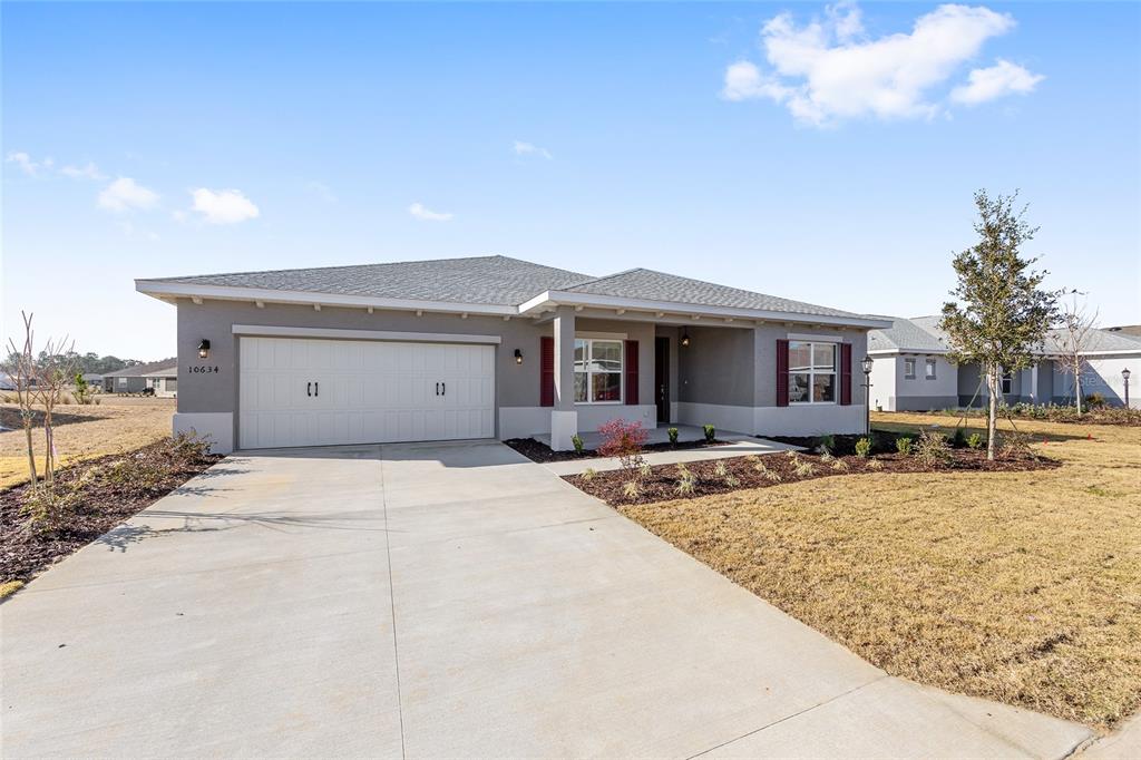 A single-story house with a two-car garage, gray stucco exterior, and a concrete driveway — 10634 SW 101ST LANE ROAD, OCALA, FL