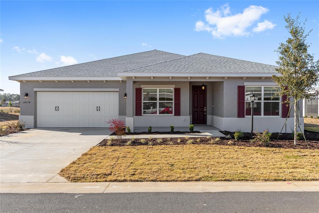 A single-story house with a two-car garage, gray stucco exterior, and red shutters — 10634 SW 101ST LANE ROAD, OCALA, FL
