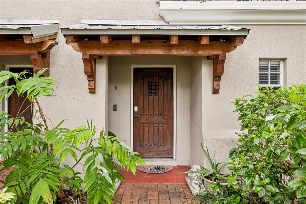 A wooden front door with a metal grille sits under a rustic timber-framed porch awning — 111 S DELAWARE AVENUE UNIT 3, TAMPA, FL