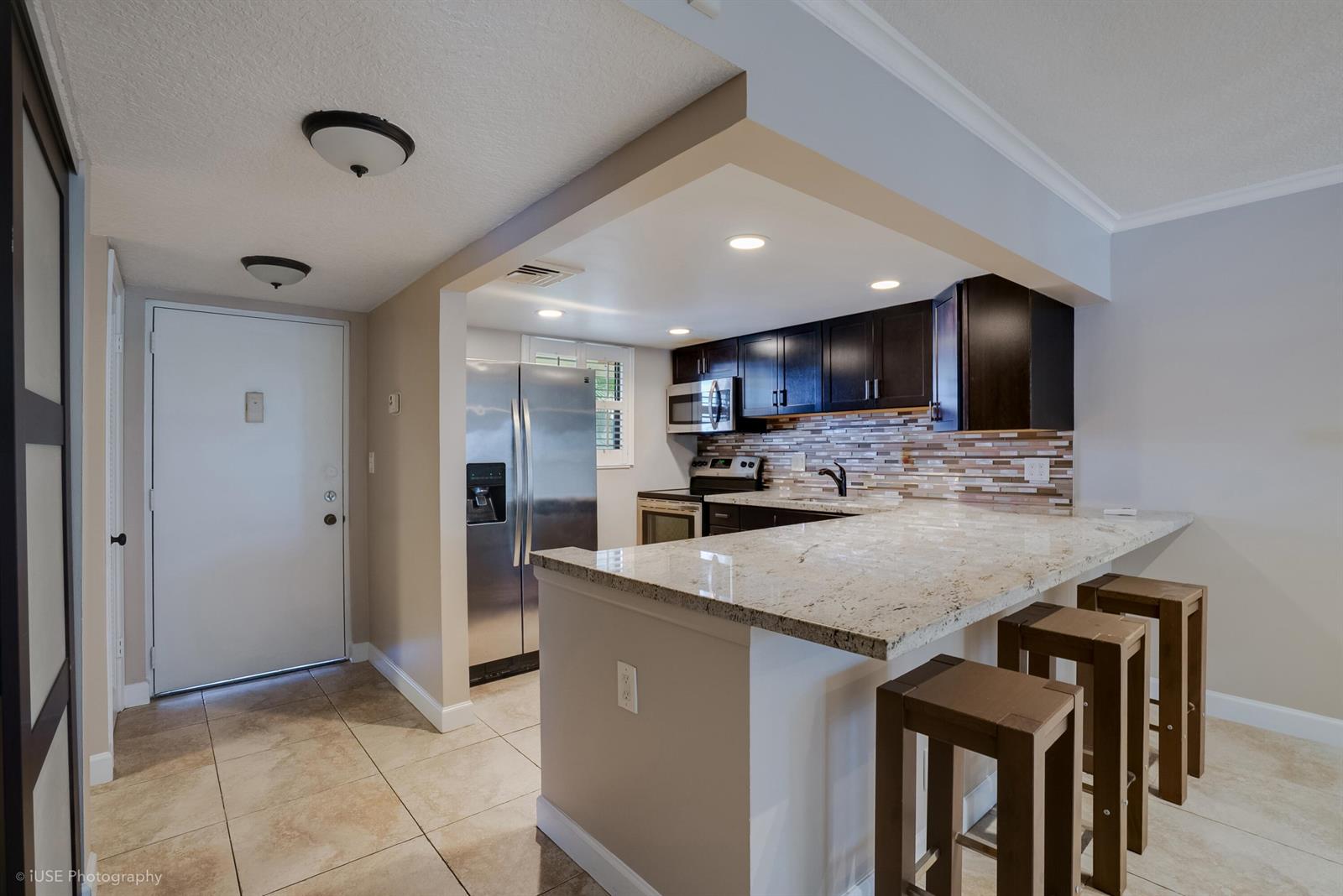 A kitchen features dark wood cabinets, granite countertops, stainless steel appliances, and a breakfast bar — 2314 S Cypress Bend Drive Unit 313, Pompano Beach FL 33069, POMPANO BEACH, FL