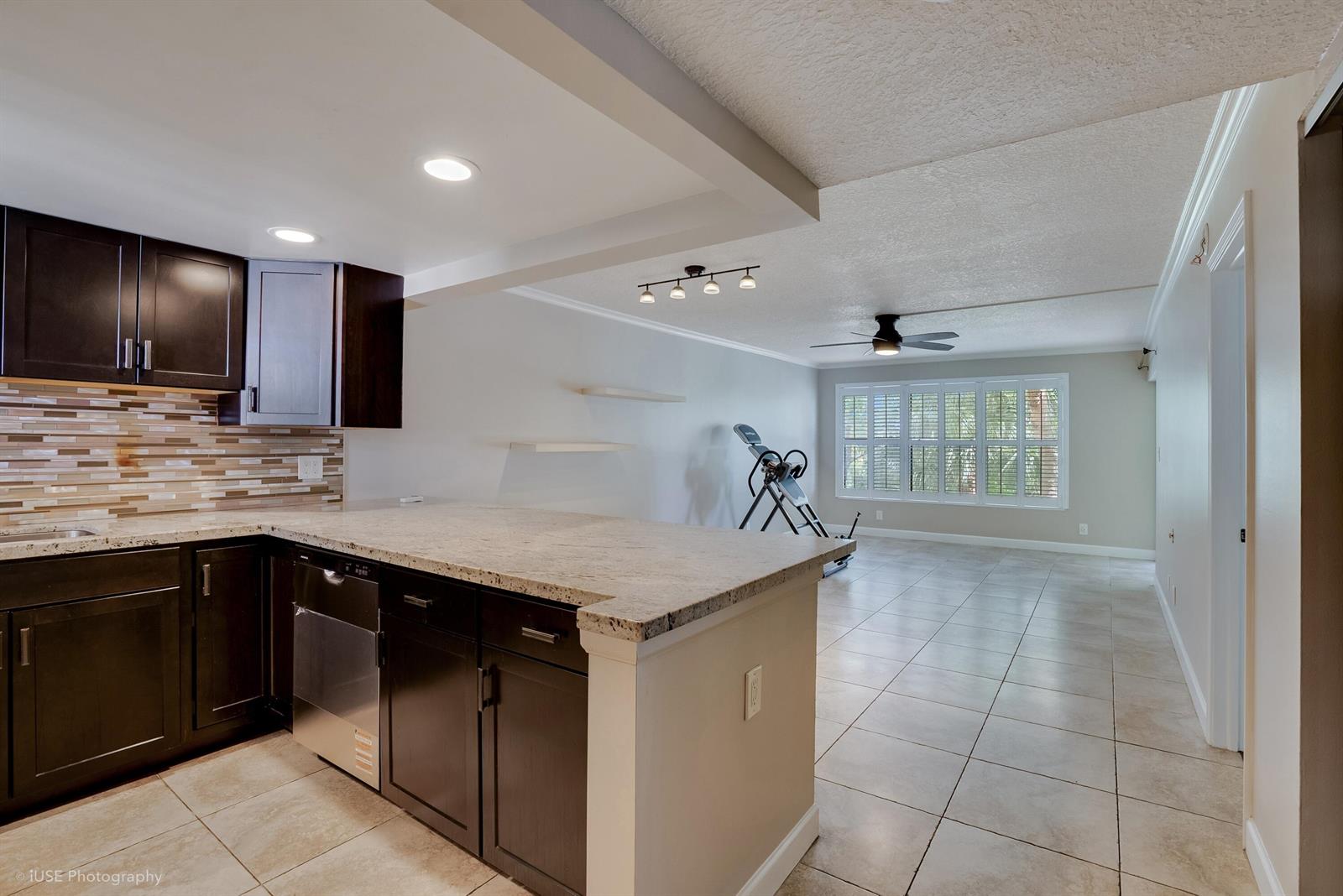 A kitchen with dark cabinets and granite countertops opens into a tiled living area — 2314 S Cypress Bend Drive Unit 313, Pompano Beach FL 33069, POMPANO BEACH, FL