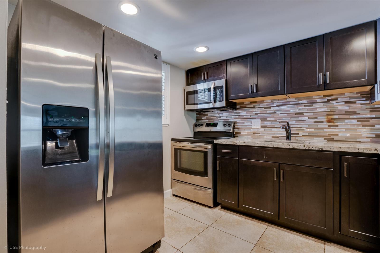 A kitchen features stainless steel appliances, dark wood cabinets, and a mosaic tile backsplash — 2314 S Cypress Bend Drive Unit 313, Pompano Beach FL 33069, POMPANO BEACH, FL