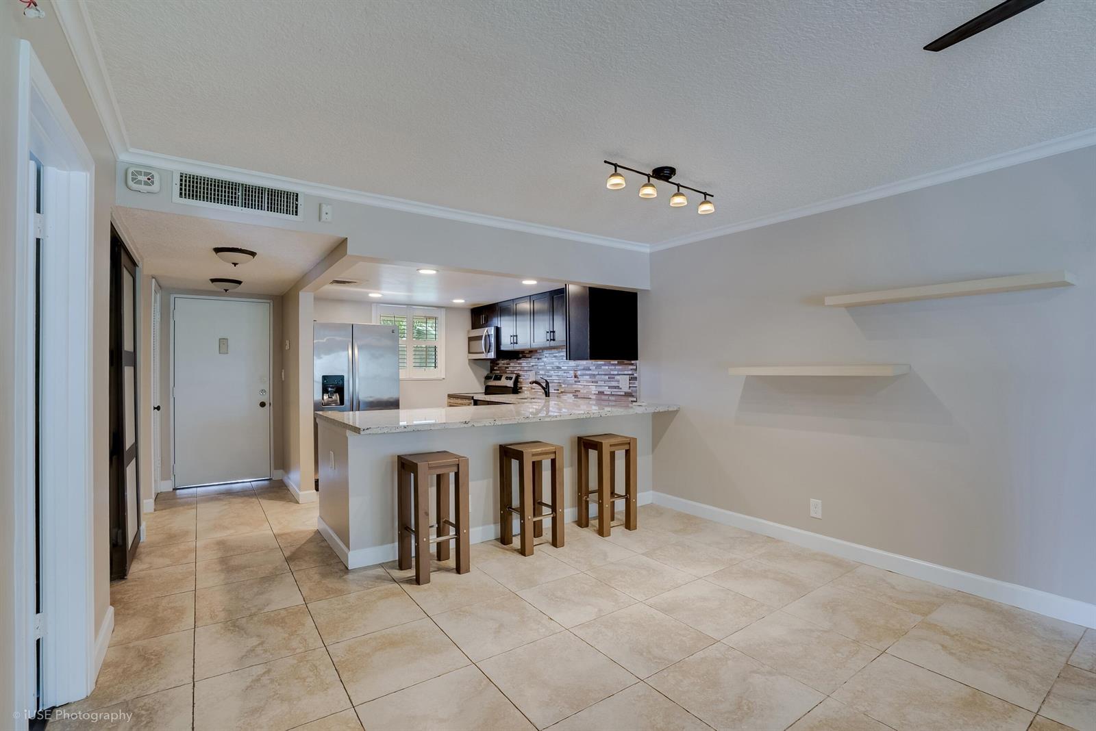 A kitchen with dark cabinets, granite countertops, and a breakfast bar opens to a dining area — 2314 S Cypress Bend Drive Unit 313, Pompano Beach FL 33069, POMPANO BEACH, FL