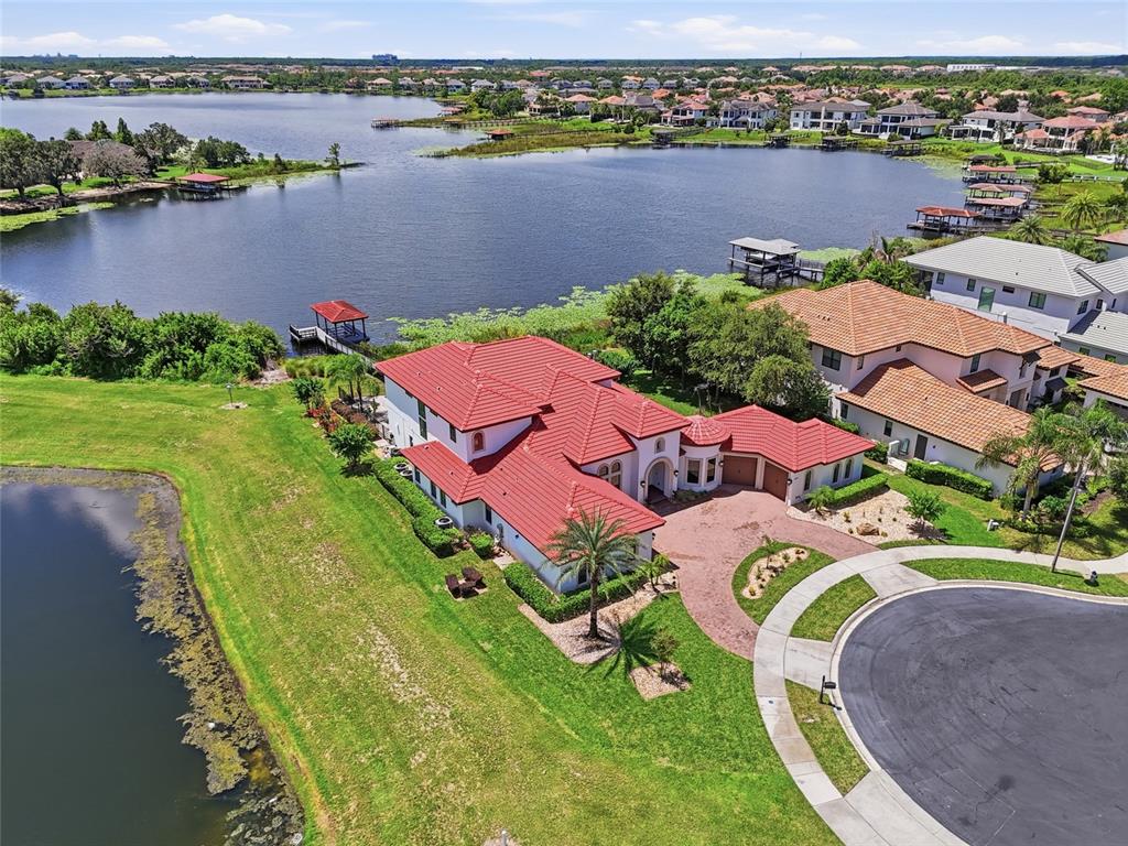 An aerial view shows a house with a red roof, pool, and dock on a lake — 12102 MONTALCINO CIRCLE, WINDERMERE, FL