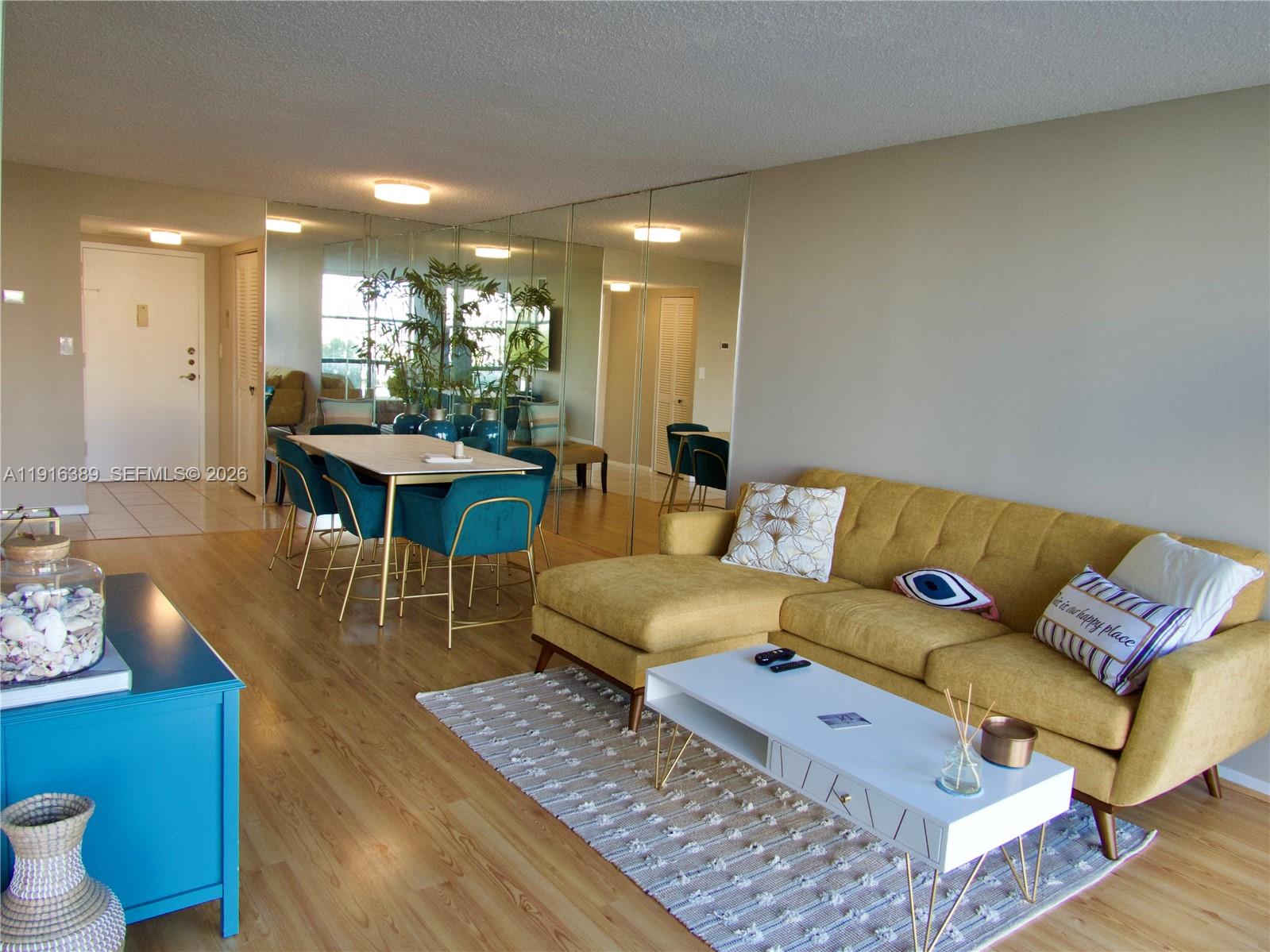 A living and dining area features a yellow sectional sofa, mirrored wall, and blue furniture — 800 Parkview Dr # 402, Hallandale Beach FL 33009, HALLANDALE BEACH, FL