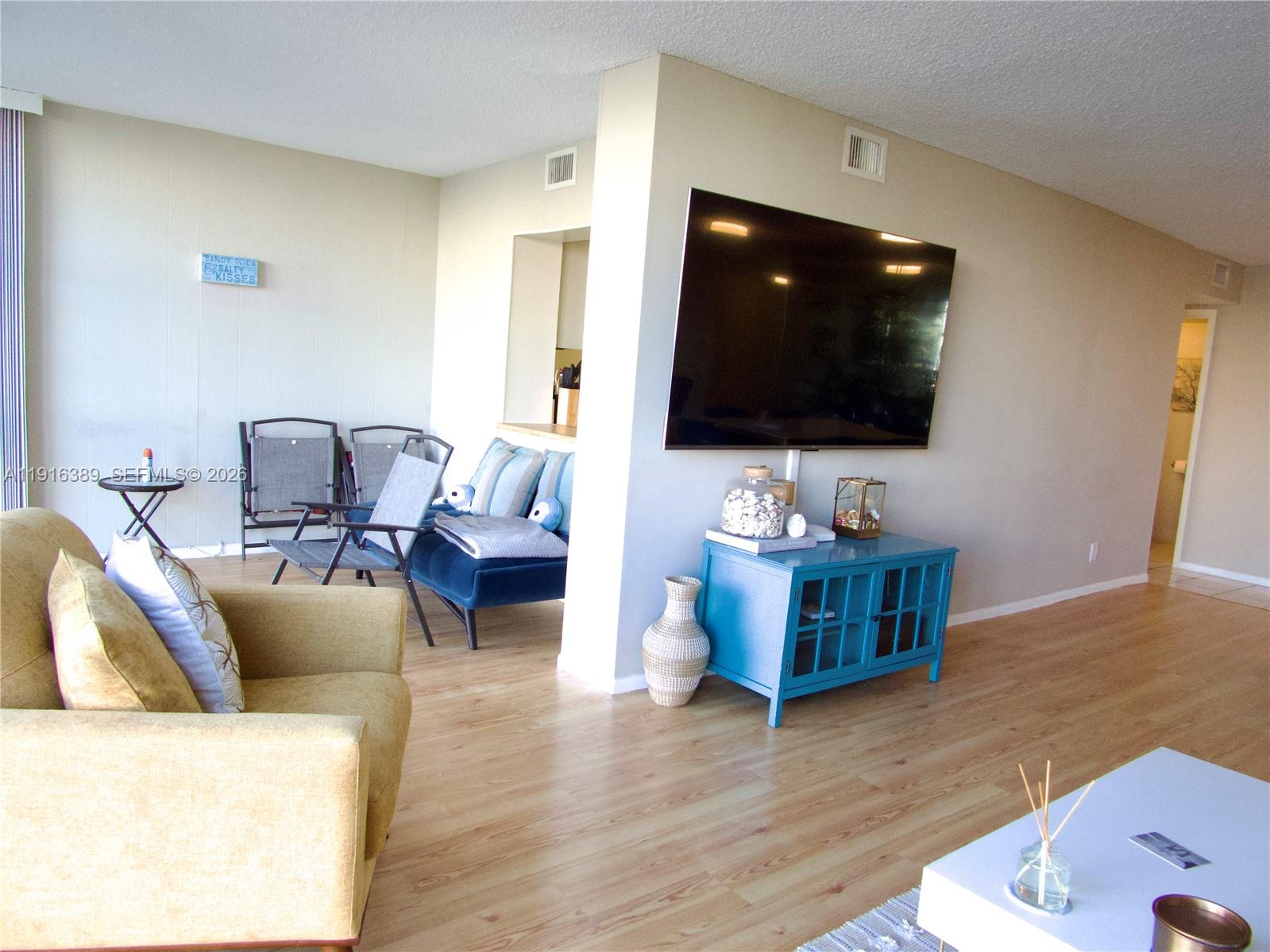 A living room features light wood flooring, a wall-mounted television, and a blue media console — 800 Parkview Dr # 402, Hallandale Beach FL 33009, HALLANDALE BEACH, FL