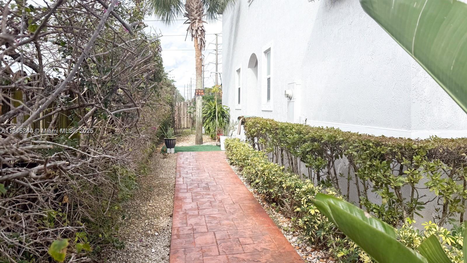 A paved walkway runs along the side of a white house next to a hedge — 1001 NE 208th St, Miami FL 33179, MIAMI, FL