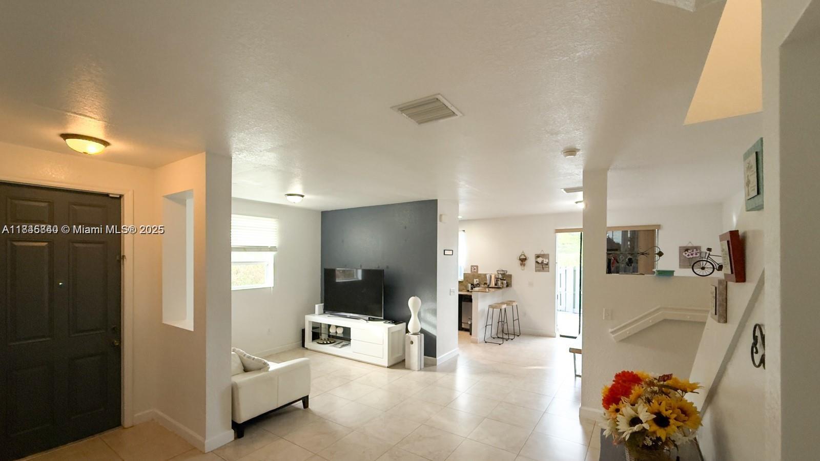 A living room with tile floors, a dark accent wall, and an adjacent kitchen area — 1001 NE 208th St, Miami FL 33179, MIAMI, FL
