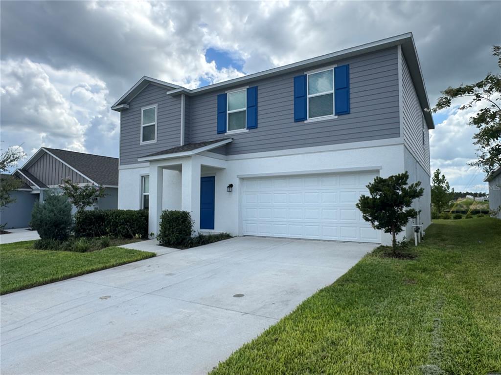 A two-story house with gray siding, blue shutters, a white garage, and a concrete driveway — 2434 MCKINLEY DRIVE, LAKE WALES, FL