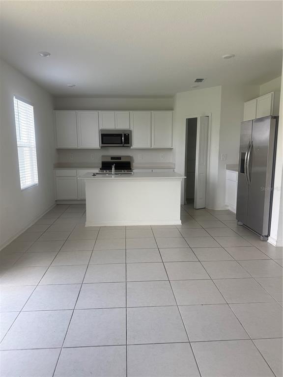 A kitchen features white cabinets, stainless steel appliances, a center island, and light tile flooring — 2434 MCKINLEY DRIVE, LAKE WALES, FL