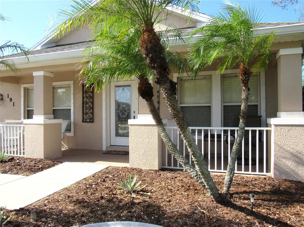 A front view of a house with a covered porch, white railings, and palm trees — 191 ALLWORTHY STREET, PORT CHARLOTTE, FL