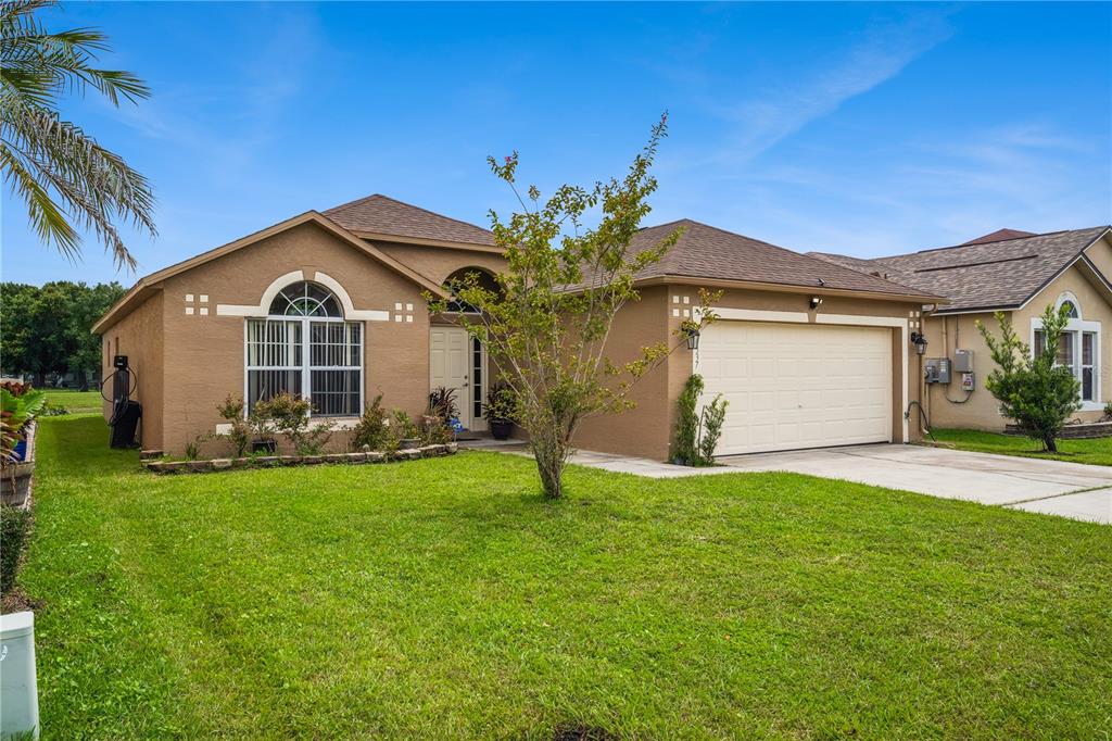 A tan single-story house with a two-car garage and a front lawn under a blue sky — 10337 LAXTON STREET, ORLANDO, FL
