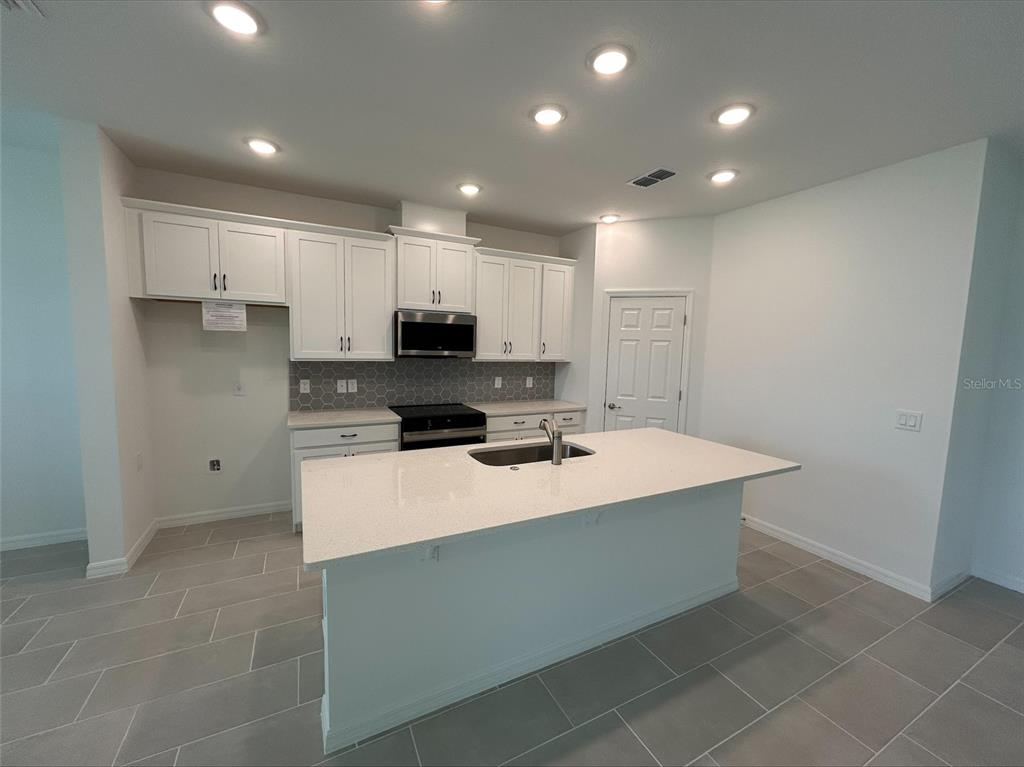 A modern kitchen features white cabinets, a central island with a sink, and gray tile flooring — 2005 EDUCATION STREET, ST CLOUD, FL