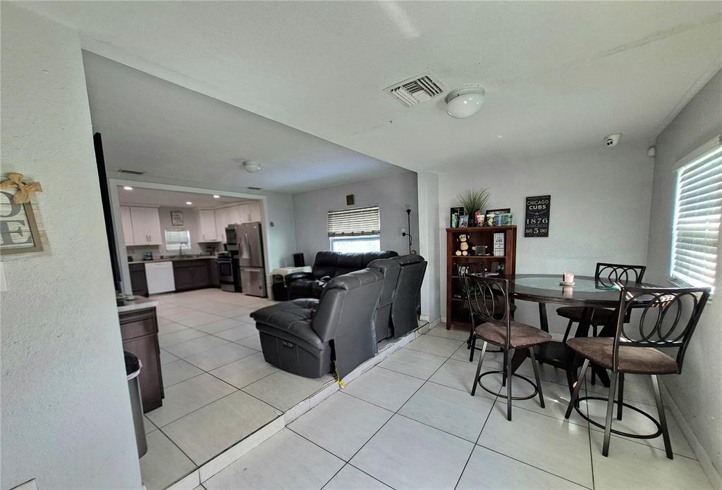 An open-concept living room and dining area with tile floors and a kitchen in the background — 709 E 119TH AVENUE, TAMPA, FL