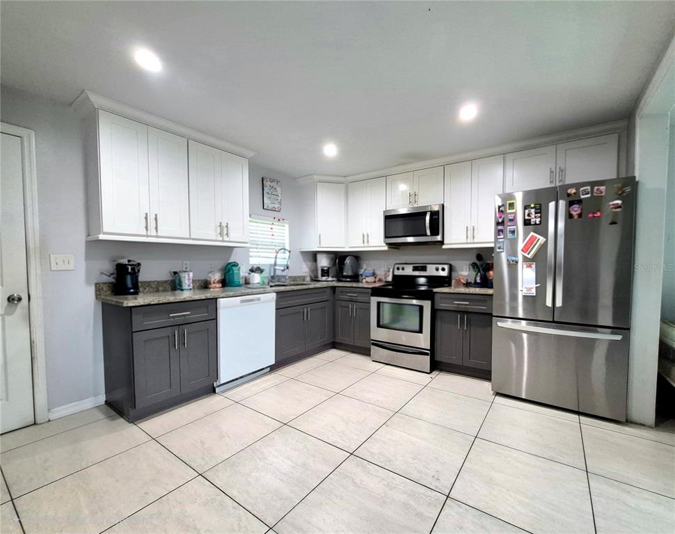 A kitchen features white upper cabinets, dark gray lower cabinets, stainless steel appliances, and tile flooring — 709 E 119TH AVENUE, TAMPA, FL