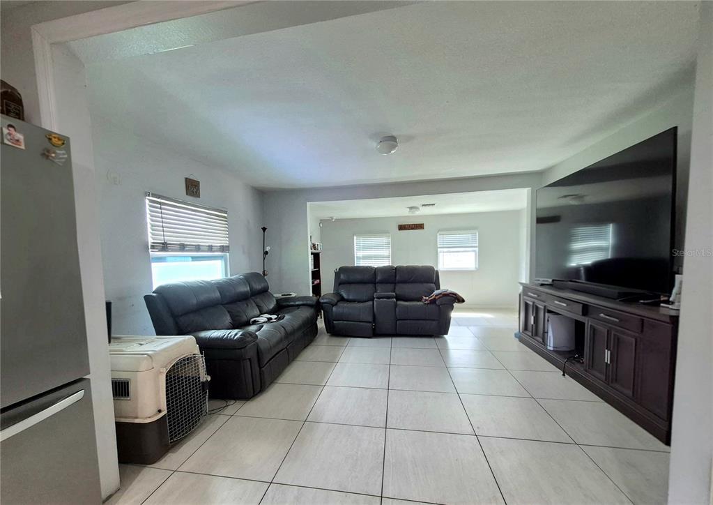 A living room features light tile flooring, two dark leather sofas, and a large television — 709 E 119TH AVENUE, TAMPA, FL