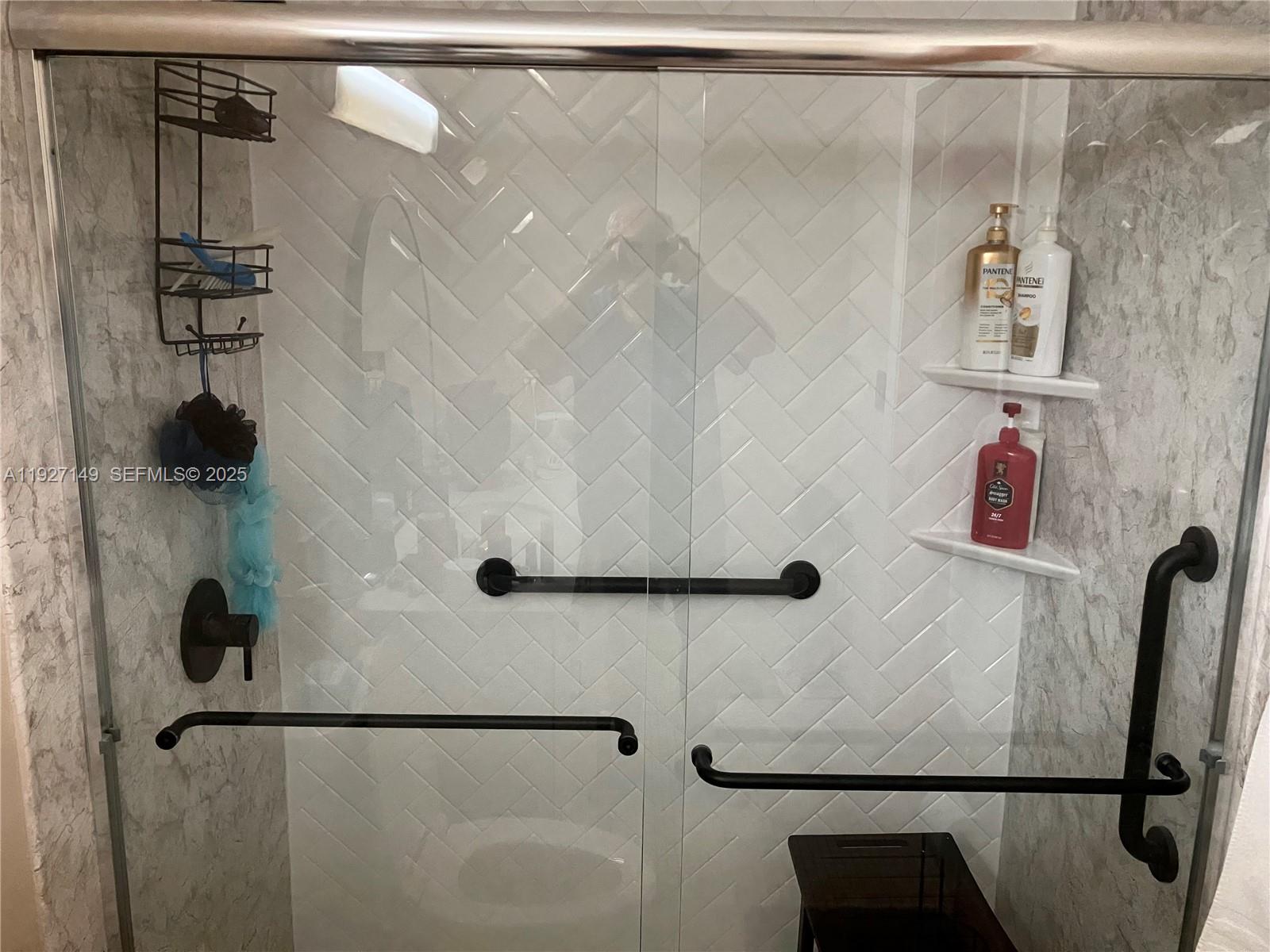 A glass-enclosed shower features white herringbone tile, black grab bars, and built-in corner shelves — 5174 Lakefront Blvd # C, Delray Beach FL 33484, DELRAY BEACH, FL
